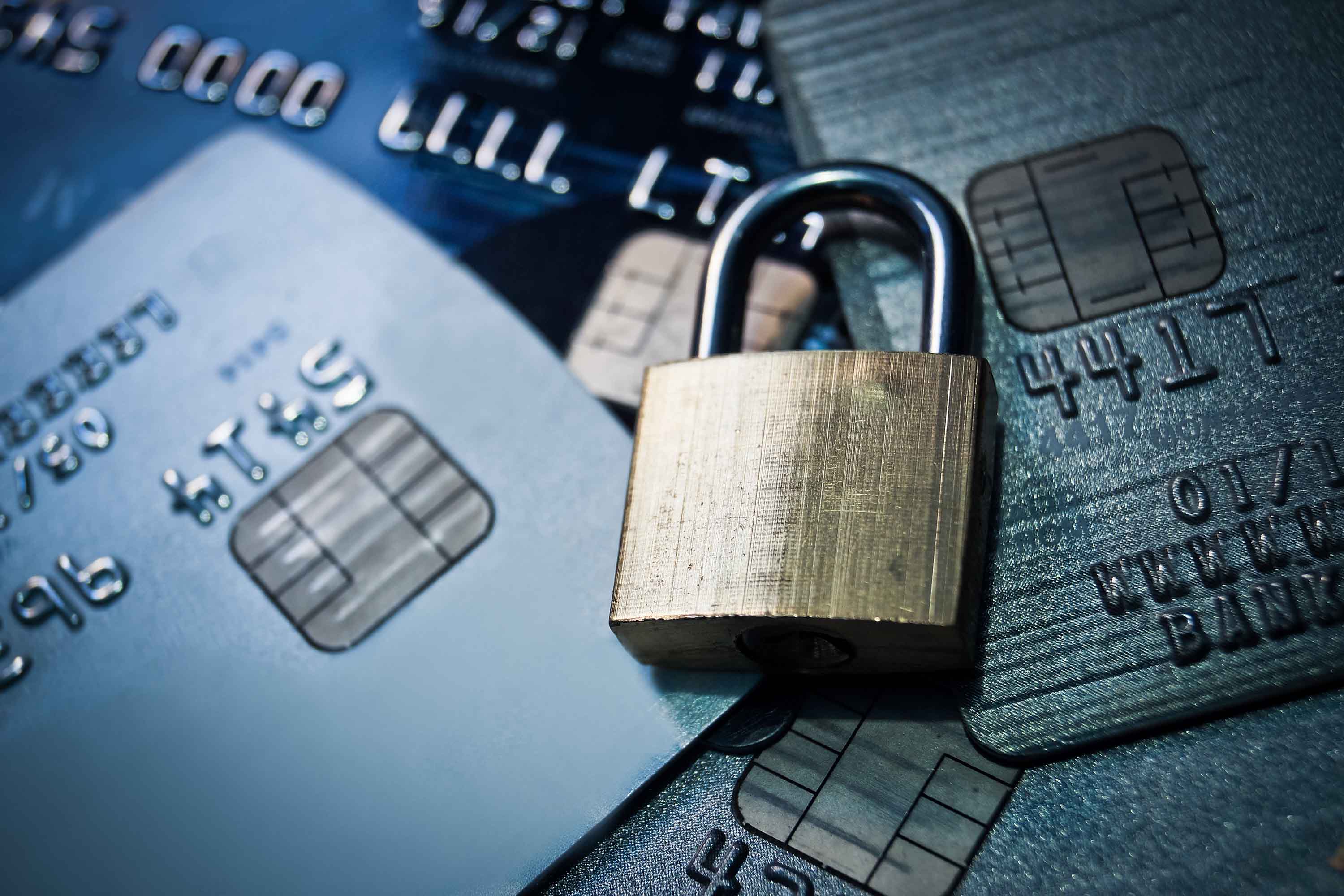 A brass padlock laying on a stack of credit cards. - patrons.com 